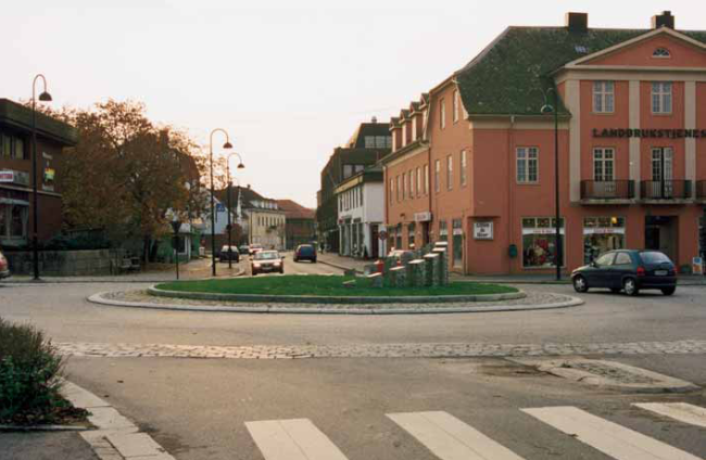 Figur 2: Rundkjøringen i miljøgaten Rakkestad. Foto: Amund Vik. Fotografi av en rundkjøring. Rundt rundkjøringen er det steinlagt, og i rundkjøringen er det en skulptur