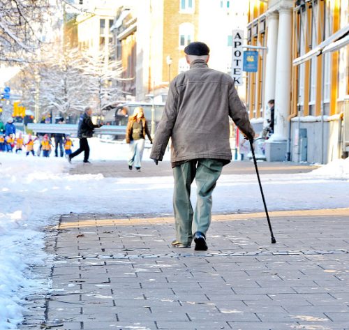 Et bilde av en gammel mann med stokk som går på islagt gangvei.