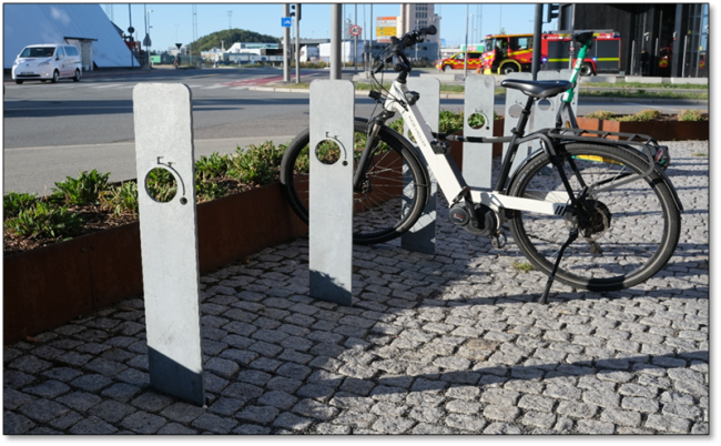 Foto av eksempel på sykkelparkering som er plassbesparende, men som gir dårlig støtte og få låsemuligheter. Stativene som er vist på bildet er flate og rettet oppover, med kun ett gjennomgående hull der det er mulighet for å feste sykkellåsen.