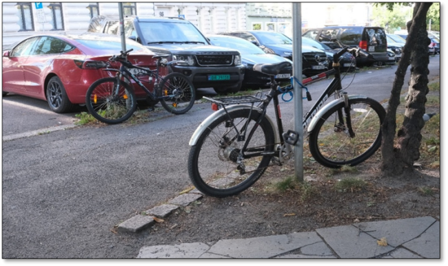 Foto viser to sykler som er låst fast til hver sin skiltstolpe. Dette er et typisk resultat av manglende tilgjengelig parkering i nærheten.