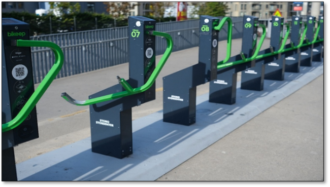 Foto som viser sykkelstativer med integrert lås ved et kjøpesenter i Oslo. Stativene er utstyrt med bøyle og QR-kode. Disse kan gi økt sikkerhet, særlig blant syklende som ikke har sikker lås selv.