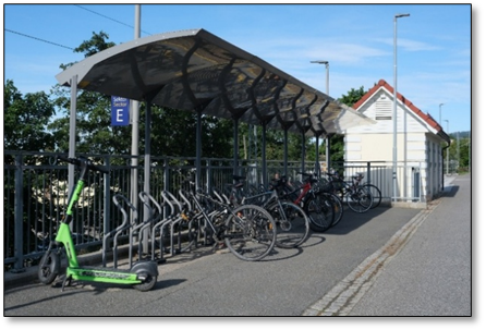 viser flere sykler parkert til Publicus stativer, plassert under et overbygget tak
