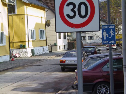 Vei i et boligområde med biler parkert langs veien og et skilt som viser at det er 30 sone, og et skilt som viser at barn leker i området.