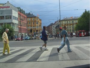 Tre personer som går over et gangfelt i et bysentrum