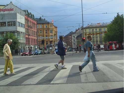 Tre personer som går over et gangfelt i et bysentrum