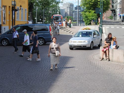 Bilde av rundkjøring og brosten-belagt bygate der biler står parkert, og folk går uforstyrret over veien i alle retninger