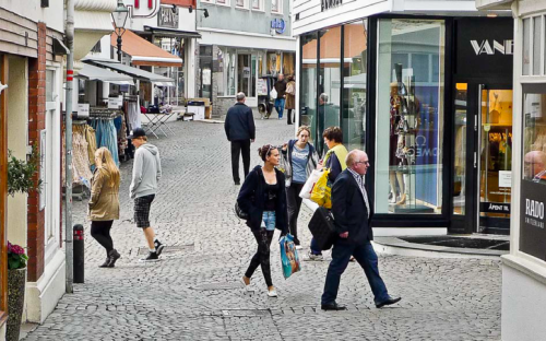 Fotoet viser en gågate, der gående ser inn gjennom vinduer til butikkene i første etasje.