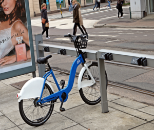 bysykkel parkert ved sykkelstativ ved en vei.