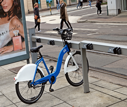 bysykkel parkert ved sykkelstativ ved en vei.