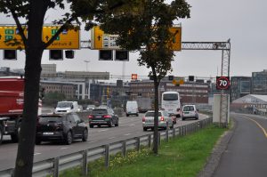 Bilde av trafikkert motorvei (E18) med overhengende skilt. Veien har fartsgrense 70 kilometer i timen.