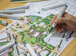 Bilde av hånd som tegner på et grafisk framstilling av by/gateplanlegging i flere farger.