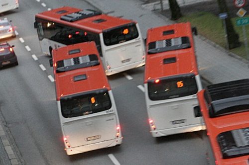 Fire røde og hvite busser på en vei.  Ser ut som de er vekslende på vei inn/ut ift busstopp.