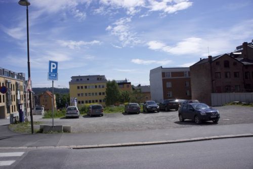 et bilde av biler parkert i en parkeringsplass ved en vei.