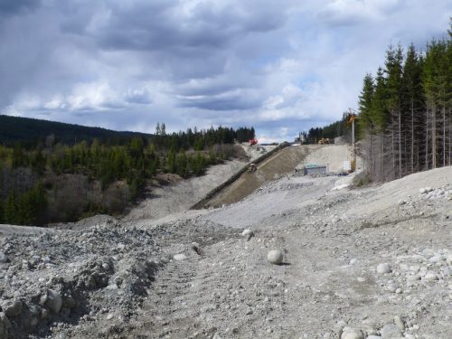 Et bilde av utbygging av en vei: store mengder grus med skog omkring.
