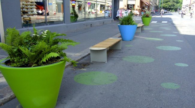 Foto av Torggata i Oslo med oppmerkede gr&oslash;nne sirkler, benker og store blomsterpotter med veietasjon i veibanen.