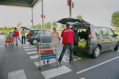 Foto bilde av en kundebil ved en "drive" der en ansatt leverer bestillingen i bagasjerommet.