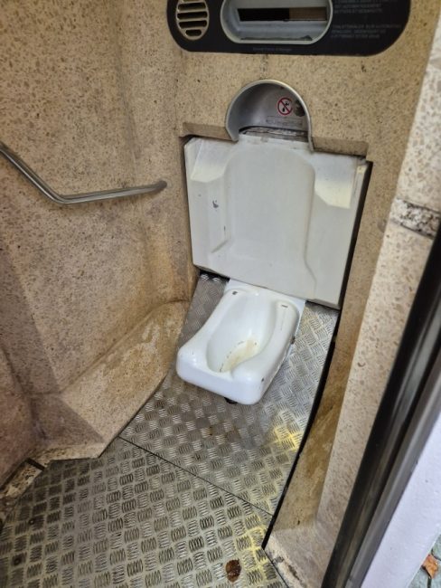 Bildet viser et toalett utenfor Stortinget hvor selve klosettet ikke ser ut som et vanlig klosset. Det har ikke toalett sete, spyleknapp eller vann. Toalettet befinner seg nede p&aring; gulvet, og det er ikke intuitivt hvordan man skal bruke det. Det er heller ingen toalettpapir eller vask.