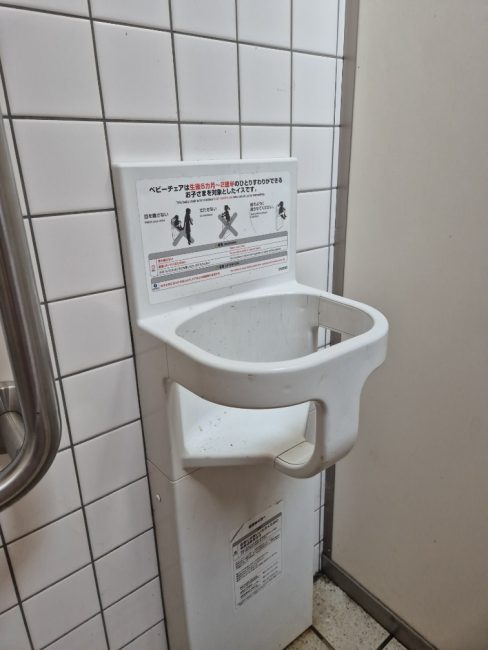 Bildet viser et offentlig toalett med en barnestol som er festet p&aring; veggen. Her er det mulig &aring; sette fra seg barnet n&aring;r man selv er p&aring; toalettet.
